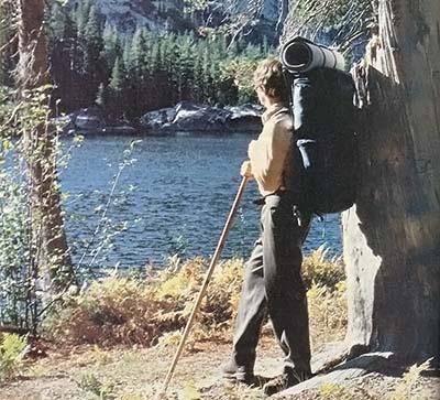 A well-prepared hiker absorbs the tranquil beauty of a mountain lake.
